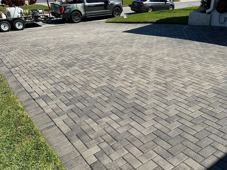 Herringbone paver driveway at a coastal home, sealed and swept, with the work trailer parked at the curb