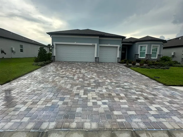 Multi-tone paver driveway immediately after a wet-look sealer application, the surface still glossy under an overcast sky