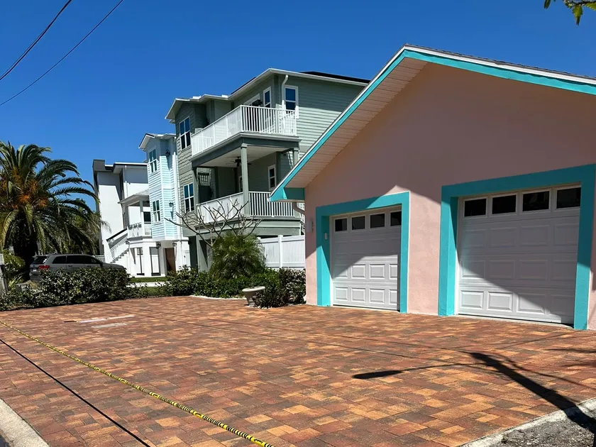 Red and tan brick paver driveway freshly sealed in front of a pastel beach cottage, roped off with caution tape while it cures