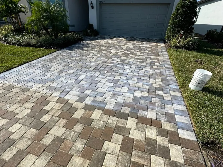 Paver driveway with the sealer application just finished, the equipment bucket still set at the edge of the field