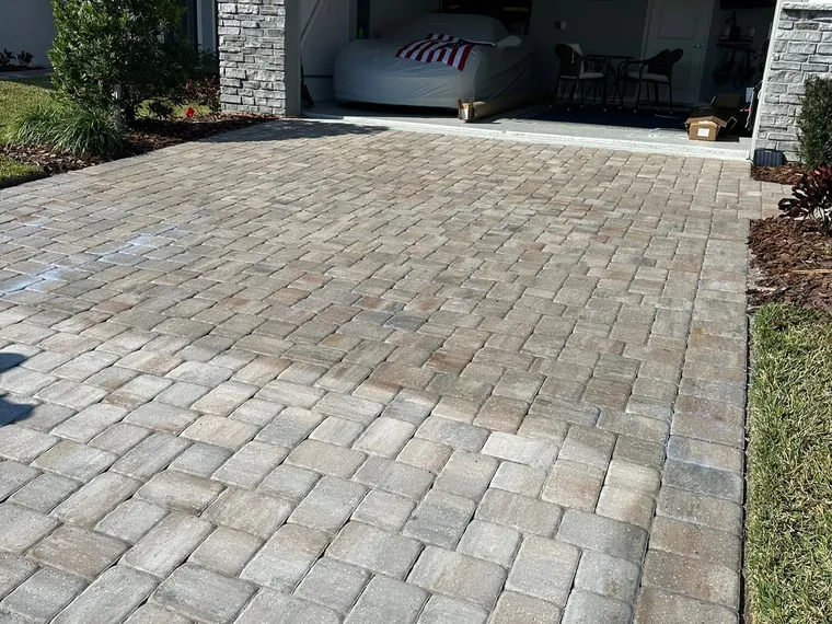 Sealed paver driveway running up to an open garage on a home with stone accent columns