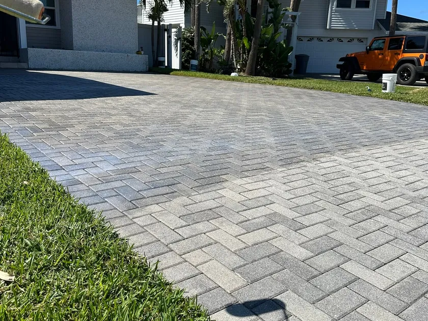Gray paver driveway at a waterfront home, sealed and clean, with a sailboat mast visible past the roofline