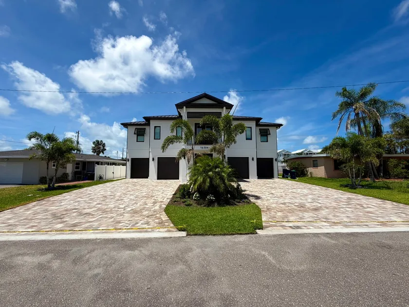 Wide paver driveway sealed to a soft sheen in front of a two-story coastal home with palms and a clear blue sky