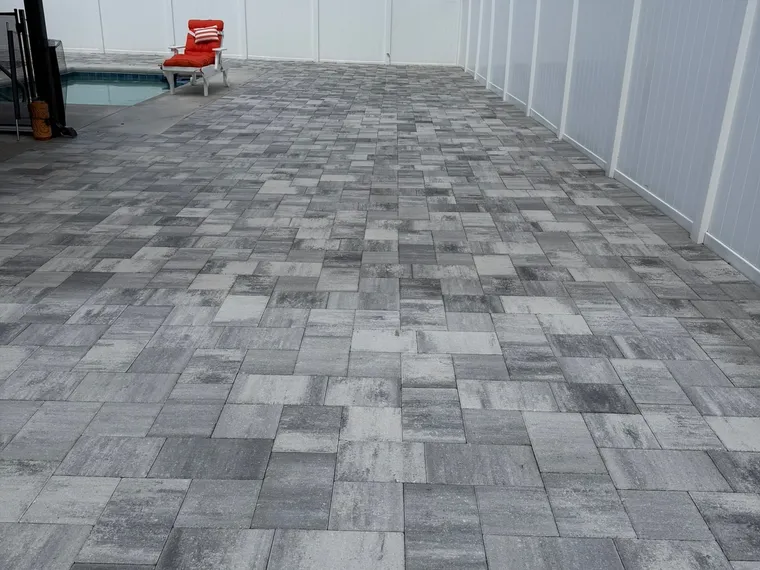 Finished gray paver pool deck extending to a white privacy fence under palms