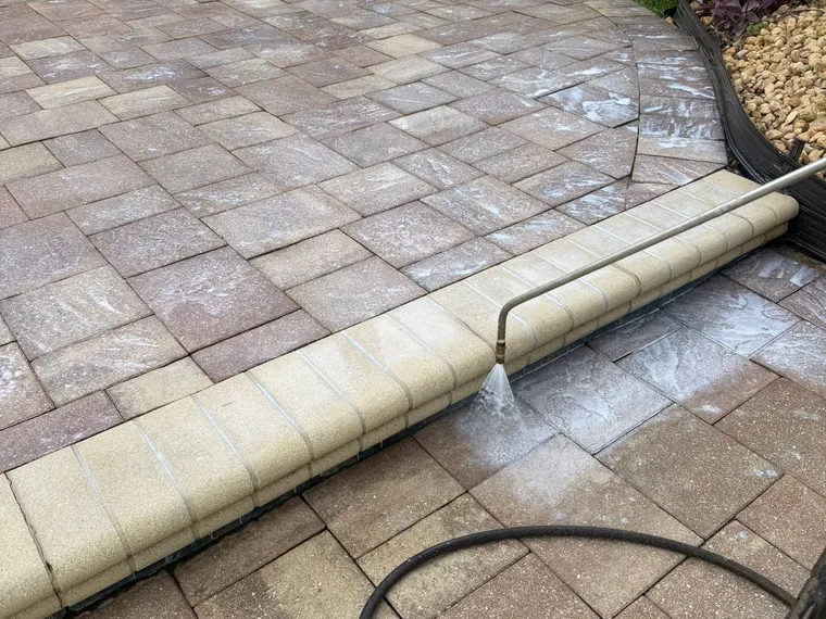 Pressure-washing hose and wand at the curved edge of a paver pool deck during cleaning