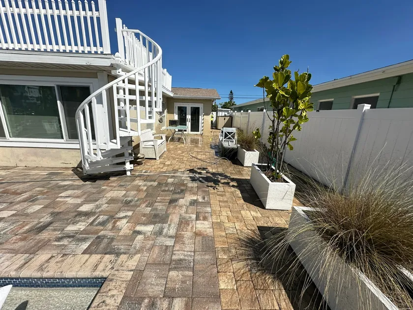 Sealed paver patio and pool deck at a beach house, with a white spiral staircase and planters along the fence line