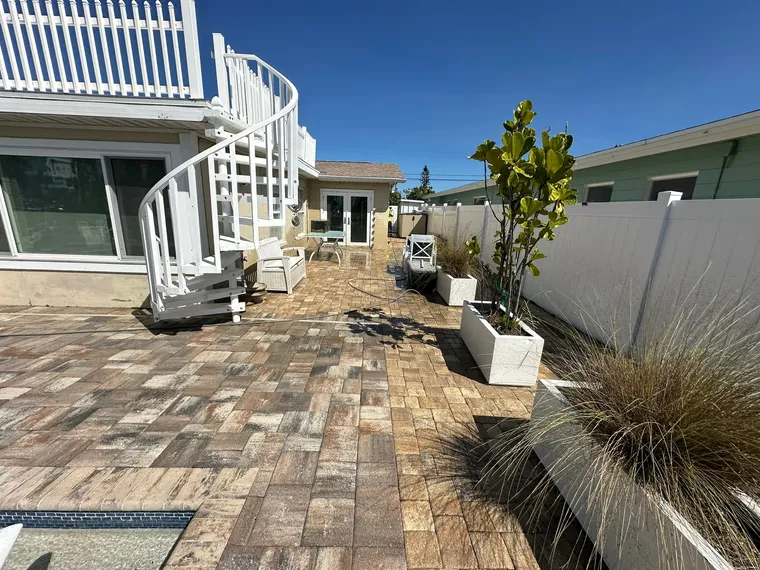 Sealed paver patio and pool deck at a beach house, with a white spiral staircase and planters along the fence line