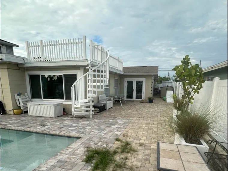 Paver pool deck before cleaning and sealing, with grass growing through open joints
