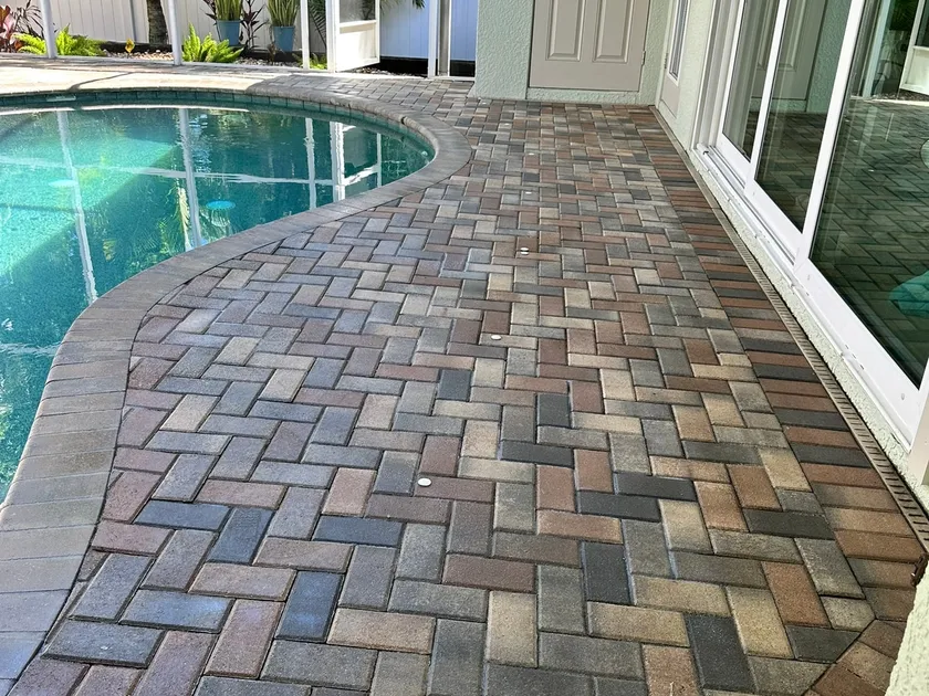 Herringbone paver pool deck inside a screen enclosure, sealed so the brown and charcoal tones read deep and even