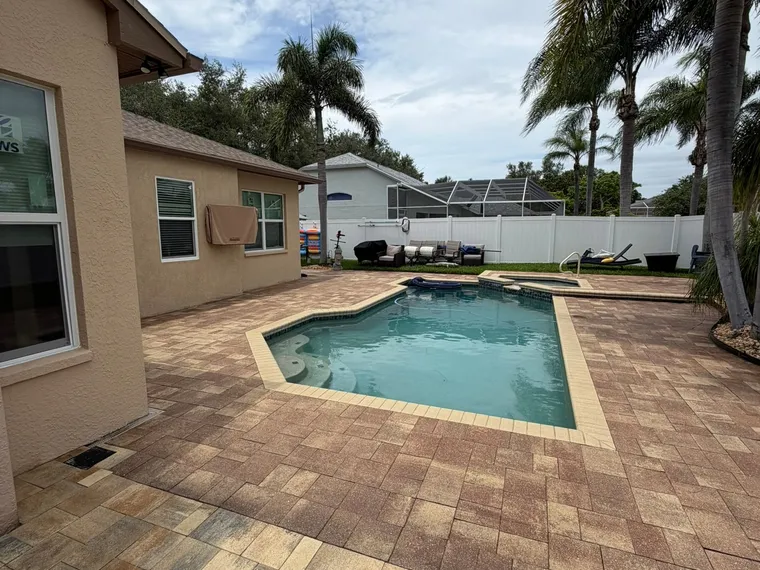 Poolside paver patio photographed from the house corner, the sealed surface holding an even color across the whole field