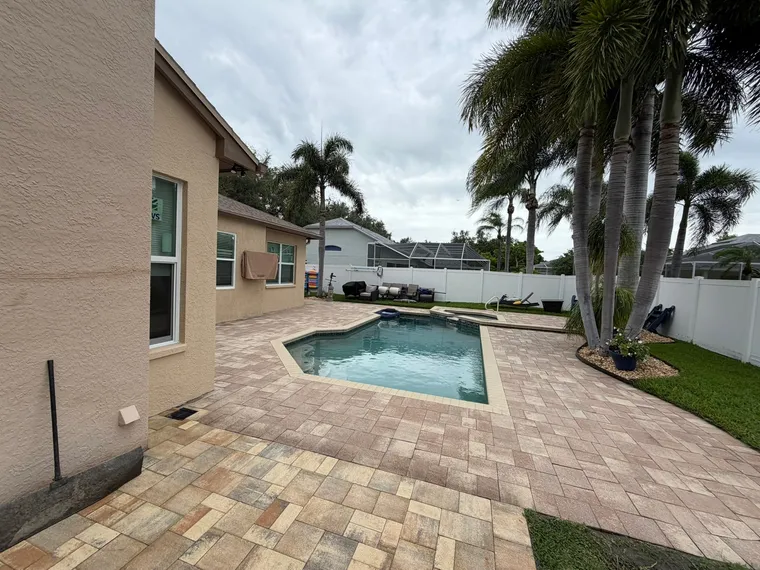 Travertine-toned paver pool deck wrapping a small backyard pool, sealed and framed by palms