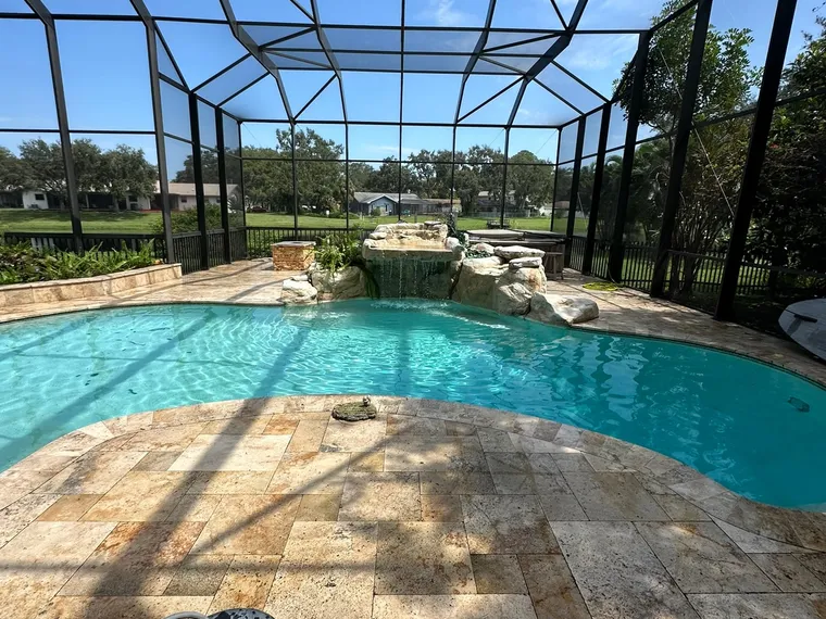 Surface cleaner working across a travertine pool deck in front of a rock waterfall