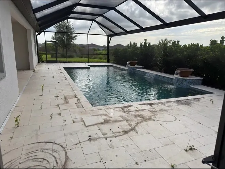 Travertine pool deck before restoration, with weeds, open joints and dark surface buildup around the pool