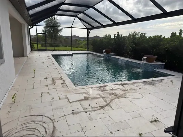 Travertine pool deck before restoration, with weeds, open joints and dark surface buildup around the pool