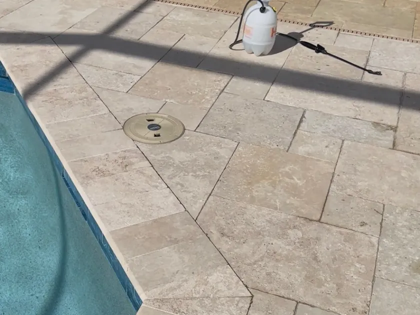 Pump sprayer staged beside a travertine pool deck before sealer application