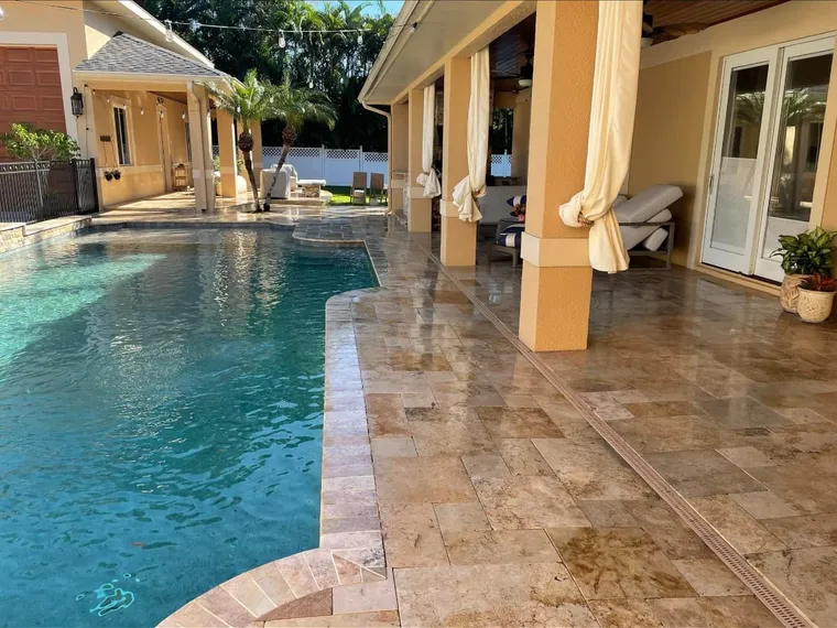 Wide travertine pool deck with an even wet-look finish around a tropical courtyard pool