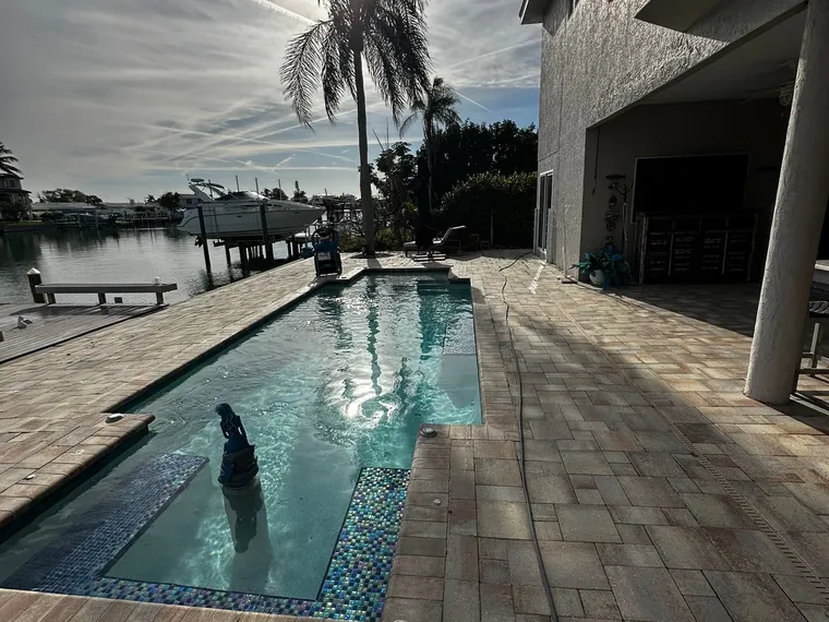 Sealed waterfront paver pool deck glowing in low afternoon sun beside a boat lift