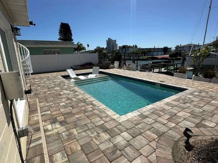 Freshly sealed paver pool deck at a waterfront home with boats and docks beyond the pool