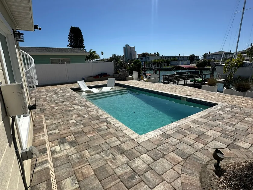 Freshly sealed paver pool deck at a waterfront home with boats and docks beyond the pool